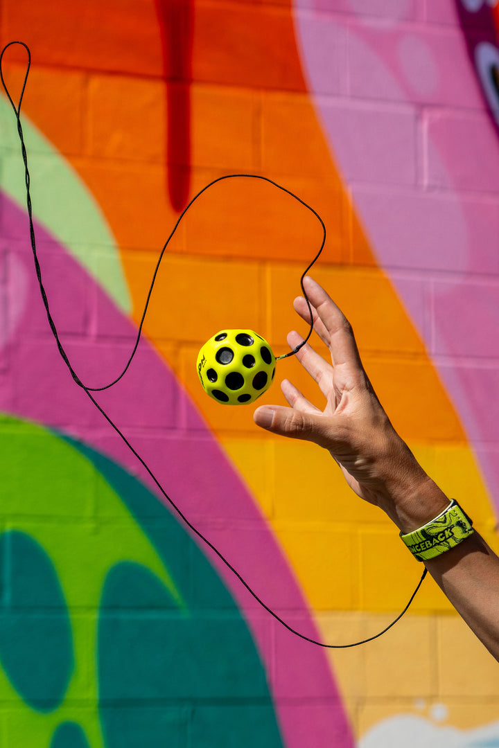 Hand holding a yellow ball with black dots against a colorful mural background