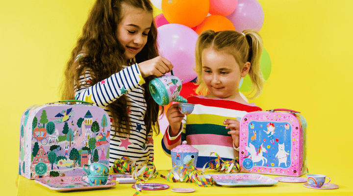 Two children playing with a tea party set against a yellow background with balloons.