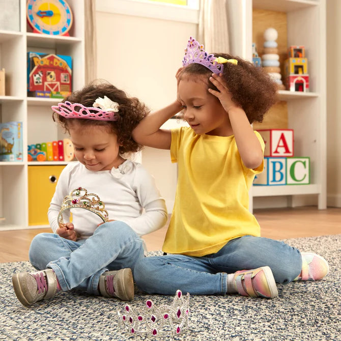 Two young girls playing with crowns in a colorful playroom.