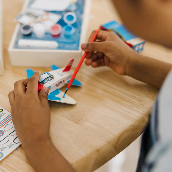Child painting a toy airplane on a wooden table