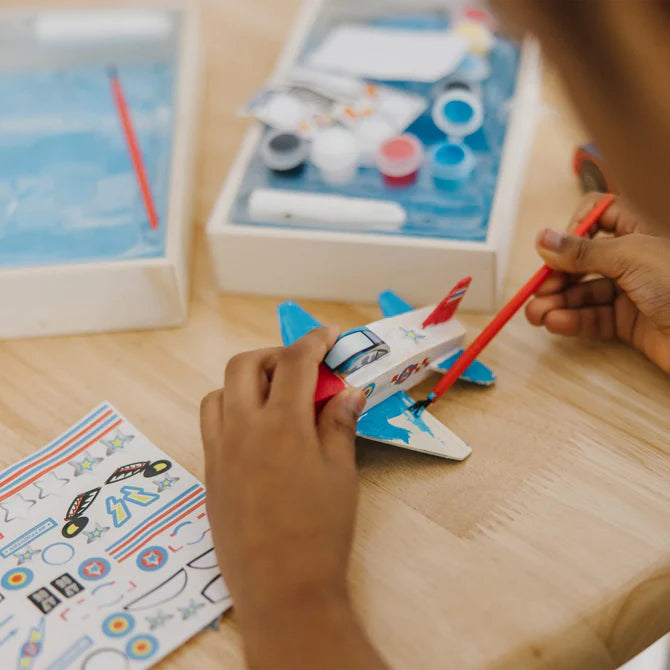 Child painting a toy airplane on a wooden table